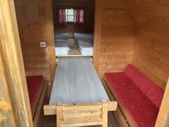 Eine gemütliche Holzhütte mit zwei roten Bänken und einem langen Tisch. Im Hintergrund sind zwei Betten sichtbar, die auf dem Boden stehen.