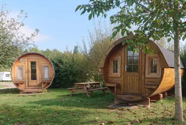 Zwei gemütliche Holzhütten im Garten, umgeben von Bäumen. Eine der Hütten hat eine Tür und Fenster, während die andere kleiner und runder ist.