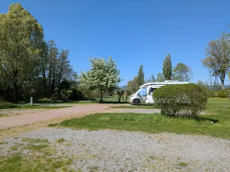 Ein schöner Campingplatz mit einem Wohnmobil und viel grünem Gras. Die Bäume und der klare blaue Himmel schaffen eine entspannte Atmosphäre.