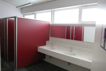 Ein modernes Badezimmer mit roten Trennwänden und Doppelwaschbecken. Helle Fenster sorgen für ausreichend Tageslicht.