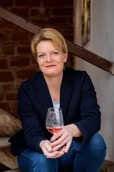 Eine Frau sitzt auf einer Treppe und hält ein Glas Roséwein. Sie trägt einen blauen Blazer und lächelt freundlich.