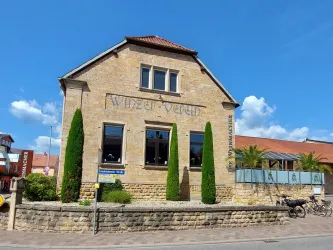 Ein charmantes Gebäude mit dem Schriftzug „Winzerverein“. Umgeben von Pflanzen und einem blauen Himmel.