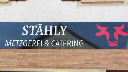 Ein auffälliges Schild mit dem Schriftzug "STÄHLY" und dem Zusatz "METZGEREI & CATERING". Es enthält ein stilisiertes Bild von Kühen in Rot.