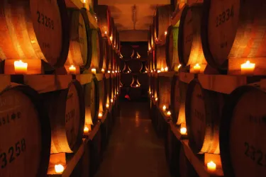 Ein gemütlicher Weinkeller mit behaglichem Licht von Kerzen. Die Regale sind voller Holzfässer, die einen Hauch von Tradition ausstrahlen.