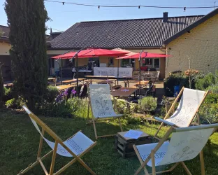 Ein gemütlicher Gartenbereich mit Liegestühlen und roten Sonnenschirmen. Im Hintergrund ist ein Haus mit einer Terrasse zu sehen.