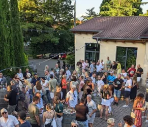 Eine große Menschenmenge versammelt sich im Freien, um gemeinsam zu feiern. Die Atmosphäre ist lebhaft und freundlich, mit einer schönen Umgebung.