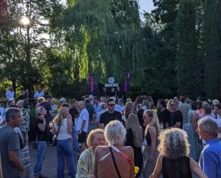 Eine lebhafte Menschenmenge bei einer Veranstaltung im Freien. Im Hintergrund ist eine Bühne mit dem Schriftzug "MOODS" zu sehen.