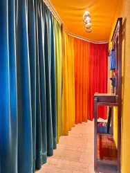 Ein farbenfroher Flur mit verschiedenen Vorhängen in Blau, Grün, Gelb, Orange und Rot. An der Wand hängen einige Gegenstände, die den Raum lebendig wirken lassen.