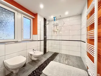 Ein modernes Badezimmer mit einer Dusche und eleganten Fliesen. Die Wände sind in Weiß und Orange gehalten, und es gibt ein großes Fenster für Tageslicht.