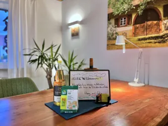 Ein Willkommensschreiben auf einem Tisch mit Getränken und Snacks. Im Hintergrund sind Pflanzen und ein beleuchteter Raum zu sehen.