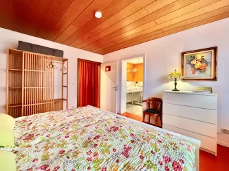 Ein gemütliches Schlafzimmer mit einem bunten Bettbezug und Holzdecke. Das Zimmer ist hell und gut eingerichtet, mit einem Stuhl und einem Nachttisch.