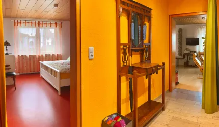 Ein einladender Flur mit orangen Wänden und einem hübschen Holzständer. Auf der linken Seite befindet sich ein Schlafzimmer mit einem Bett und Fenster.