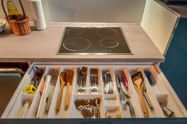 Eine moderne Küchenschublade mit verschiedenen Kochutensilien und Besteck. Darauf befindet sich ein Glaskochfeld.