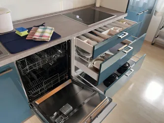 Eine moderne Küche mit blauen Schränken und einem Geschirrspüler. Die Schubläden sind teilweise geöffnet und enthalten Geschirr sowie Küchenutensilien.