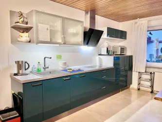 Eine moderne Küche mit grünen Schränken und hellem Arbeitsbereich. Es gibt verschiedene Küchengeräte sowie eine Fensterfläche, die für natürliches Licht sorgt.