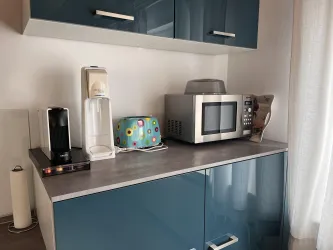 Eine moderne Küchenzeile mit blauen Schränken. Auf der Arbeitsplatte stehen eine Mikrowelle, eine Kaffeemaschine und ein Wasserkocher.