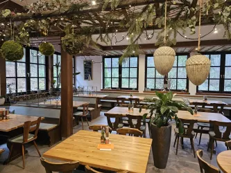 Ein modernes Restaurant mit Holzmöbeln und großen Fenstern. Die Innenausstattung ist mit Pflanzen und dekorativen Elementen geschmückt.