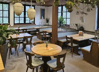 Ein gemütliches Restaurant mit Holztischen und Stühlen. Die Atmosphäre wird durch Pflanzen und warme Beleuchtung ergänzt.