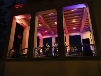 Eine Band spielt auf der Terasse von Schloss Villa Ludwigshöhe. Bunte Lichter beleuchten die Szene bei Nacht.