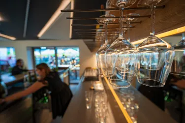 Eine moderne Bar mit hängenden Weingläsern. Im Hintergrund sind Gäste und eine angenehme Atmosphäre zu sehen.