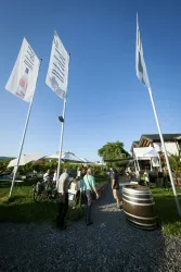 Ein erholsamer Außenbereich mit Gästen, die sich treffen. Im Hintergrund sind große Schilder und ein Gebäude zu sehen, umgeben von grüner Landschaft.