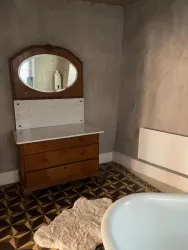 Ein schlichtes Badezimmer mit einem Holzmöbel und einem Spiegel. Der Boden ist mit geometrischen Fliesen gestaltet.