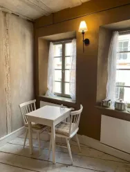 Ein gemütlicher Essbereich mit einem kleinen, weißen Tisch und zwei Stühlen. Große Fenster mit Vorhängen sorgen für viel Tageslicht in einem schlicht gestalteten Raum.