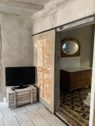 Ein gemütliches Zimmer mit einem Fernseher auf einem Holzkasten. Im Hintergrund ist eine Kommode und ein Spiegel in einem stilvollen Raum zu sehen.