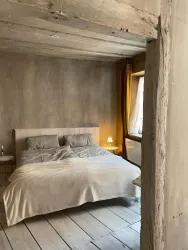 Ein gemütliches Schlafzimmer mit einem großen Bett und weich fallenden Decken. Helle Wände und ein Fenster mit gelben Vorhängen schaffen eine einladende Atmosphäre.