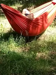 Eine rote Hängematte im Grünen. Ein Mensch liegt entspannt darin und genießt die Sonne.