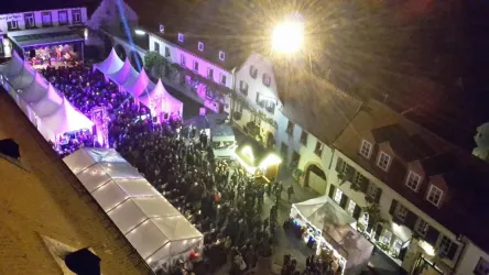 Ein belebter Platz bei Nacht mit vielen Menschen. Bunte Lichter und Zelte schaffen eine festliche Atmosphäre.