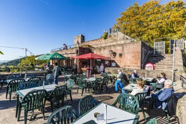 Eine Café-Terrasse mit vielen Tischen und Stühlen im Freien, umgeben von bunten Schirmen. Im Hintergrund sind Menschen zu sehen, die die Aussicht genießen.