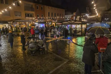 Ein festlicher Weihnachtsmarkt bei Nacht mit festlicher Beleuchtung. Viele Menschen genießen die Atmosphäre und die Stände auf dem Platz.