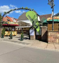 Ein einladendes Restaurant mit einer Terrasse und einem grünen Schirm im Freien. Der Eingangsbereich ist freundlich gestaltet und lädt zum Verweilen ein.