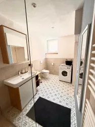 Ein modernes Badezimmer mit einer Dusche, einem Waschbecken und einer Waschmaschine. Der Boden ist mit dekorativen Fliesen gestaltet und es gibt einen großen Spiegel.