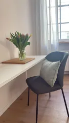 Ein moderner Schreibtisch mit einer Vase voller Tulpen und einem Kissen auf dem Stuhl. Der Raum ist hell und freundlich mit natürlichem Licht.