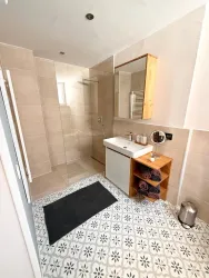 Ein modernes Badezimmer mit einer großen Dusche und einem Waschbecken. Der Boden ist mit dekorativen Fliesen gestaltet und es gibt einen Holzschrank für Handtücher.