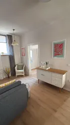 Ein helles Wohnzimmer mit modernem Mobiliar und warmen Holzböden. Es gibt einen gemütlichen Sessel und einen eleganten Sideboard mit dekorativen Elementen.
