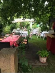 Ein einladender Garten mit Tischen und Stühlen unter Bäumen. Die Atmosphäre ist freundlich und gemütlich.