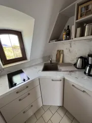 Eine moderne Küche mit einer hellen Arbeitsplatte und einer Spüle. Es gibt auch einen kleinen Herd und eine Kaffeemaschine.