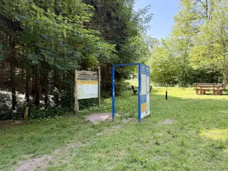 Ein ruhiger Platz in der Natur mit einer Informationsstelle und einem Picknicktisch. Umgeben von Bäumen und grünem Gras.