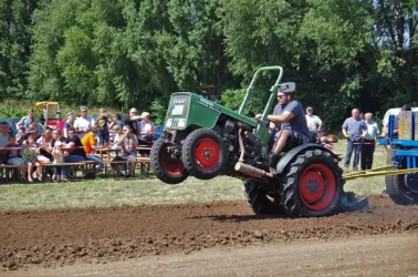 Ein Traktor hebt im Wettbewerb das Vorderrad an. Zuschauer beobachten fasziniert das Geschehen auf dem Feld.