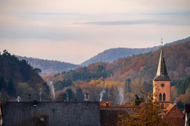 Eine malerische Landschaft mit sanften Hügeln und herbstlichen Farben. Im Vordergrund ist eine Kirche mit einem hohen Turm zu sehen.