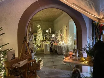 Ein festlich dekorierter Raum mit Weihnachtsbaum und Lichtern. Der Eingang ist von einem schlichten Bogen umrahmt und vermittelt eine gemütliche Atmosphäre.