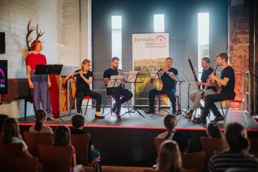 Eine Gruppe von Musikern spielt auf der Bühne, während das Publikum aufmerksam zusieht. Im Hintergrund ist ein Banner mit dem Schriftzug „Bühne frei für alle“ zu sehen.