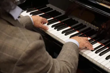 Ein Musiker spielt Klavier. Die Hände sind über den Tasten angeordnet und der Fokus liegt auf der Musik.