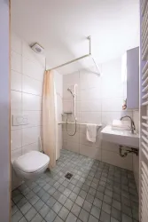 Ein modernes Badezimmer mit Dusche und WC. Die Wände sind hell gefliest und der Boden hat quadratische Fliesen.