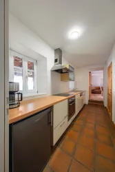 Eine moderne Küche mit Holzarbeitsplatte und Edelstahlgeräten. Der Raum hat helle Wände und Fliesenboden, mit Fenster für natürliches Licht.