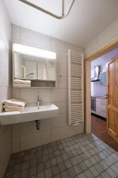 Ein modernes Badezimmer mit einem Waschbecken, einem Spiegel und einem Handtuchhalter. Im Hintergrund ist eine offene Tür zur Küche zu sehen.