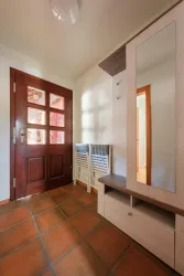 Ein einladender Eingangsbereich mit einer braunen Tür und einem großen Spiegel. Neben der Tür stehen zwei Stühle und ein Schuhschrank.